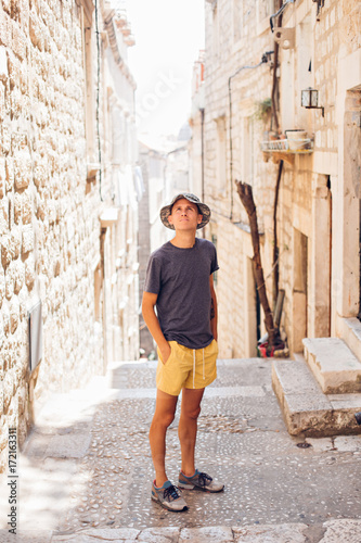 Handsome attractive young man in yellow shorts and panama hat, walks around old european town in summer heat, explores ancient tourist attractions
