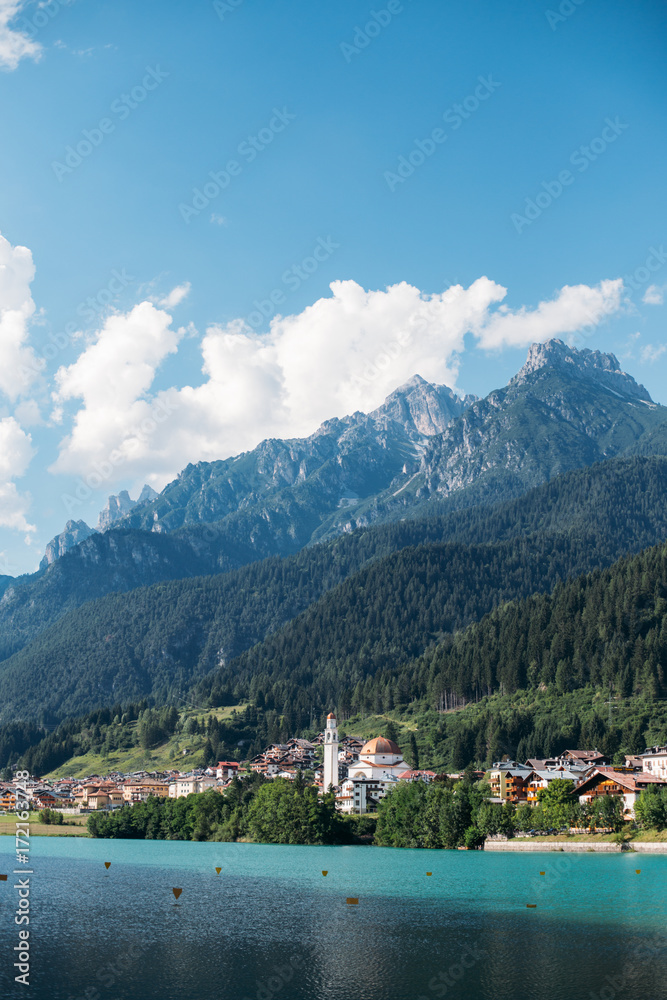 View over beautiful pristine italian village lost high in mountains, with tremendous huge rock range over old town, blue skies with white clouds over dolomites