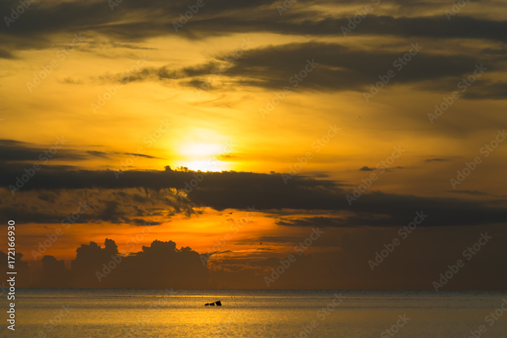 The sun shines through the clouds at dawn on the shore of the Gulf of Thailand.