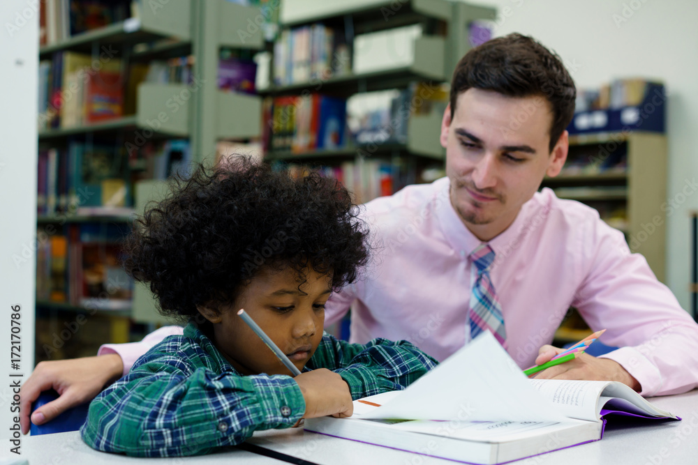 Naklejka premium Portrait of teacher assisting little boy with homework in the library