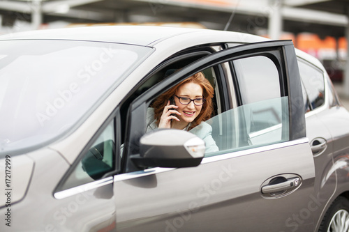 Attractive red hair businesswoman getting out of car and talking on phone.