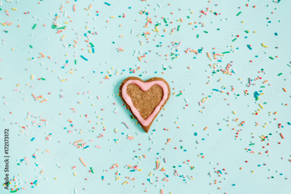Colorful hand made heart symbol cookie and confetti on blue background. Flat lay, top view. Colorful hand made heart symbol cookie and confetti on blue background. Flat lay, top view.