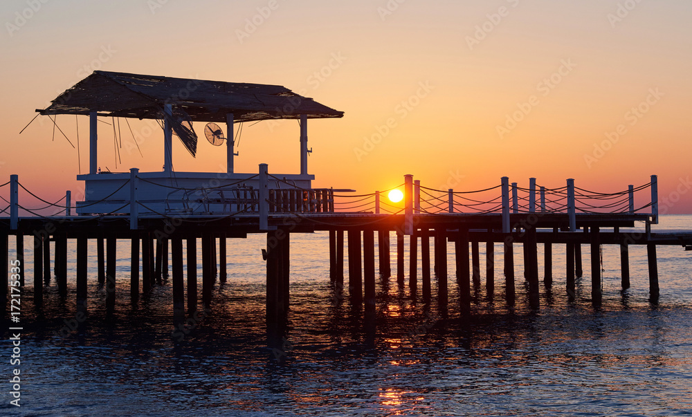 gazebo on the wooden pier into the sea with the sun at sunset