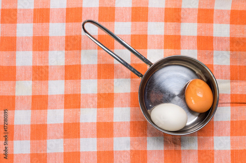 Two eggs in saucepan on checered towel photo