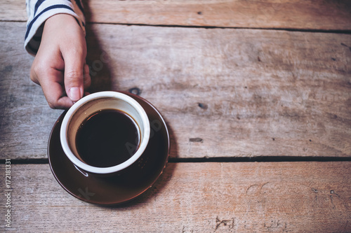 Top view image of a woman's hand holding a cup of hot coffee on vintage wooden table background