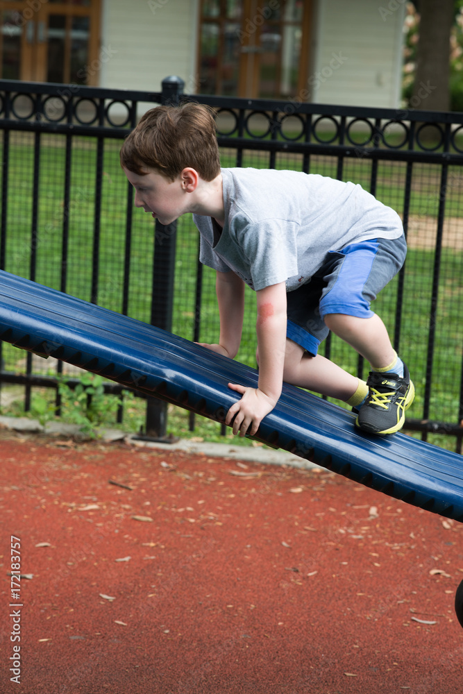Young boy having fun outside at park on a playground climbing set