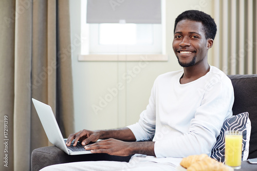 Young freelancer with laptop sitting in armchair and networking at home