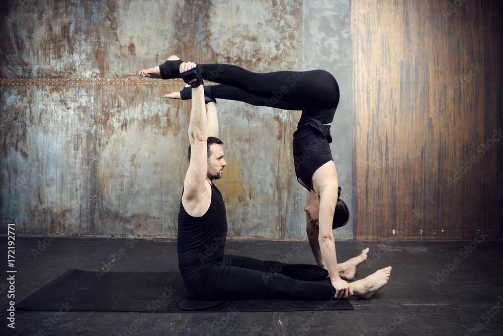 Young athletic couple practicing acroyoga. Balancing in pair. Fit