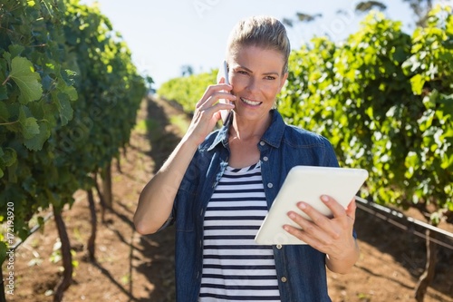 Female vintner using digital tablet while talking on mobile