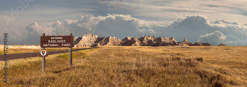 Landscape panorama of badlands Rocky Mountain range, clouds, and grassland with sign photo