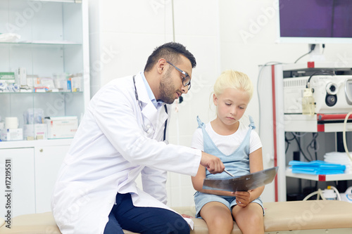 Little girl looking at x-ray image while doctor explaining it
