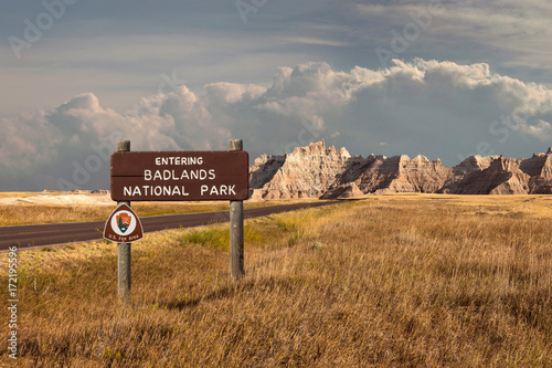 Beautiful landscape of badlands entering wood sign with clouds and large mountain range butte photo