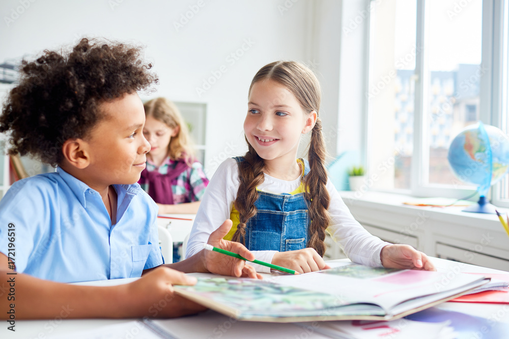 Friendly classmates with open book of tales having discussion on background of schoolboy