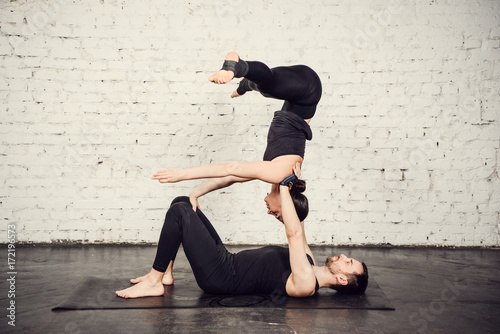 Young athletic couple practicing acroyoga. Balancing in pair. Fit active pair yoga time. Sporty handsome man supporting and holding slim beautiful brunette woman. Training time. Asana 