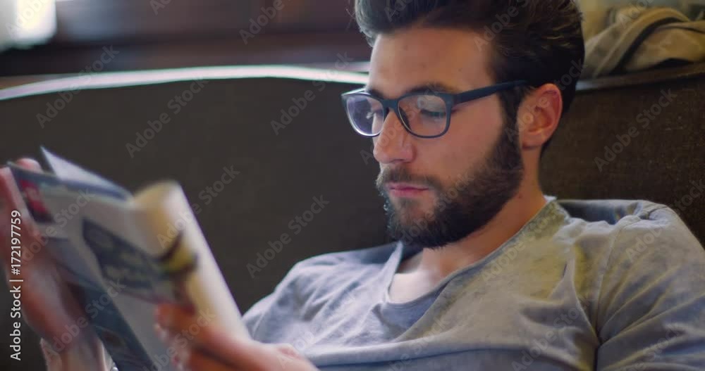 Youg millennial man relaxing reading magazine newspaper at home in casual dressing. 4k video