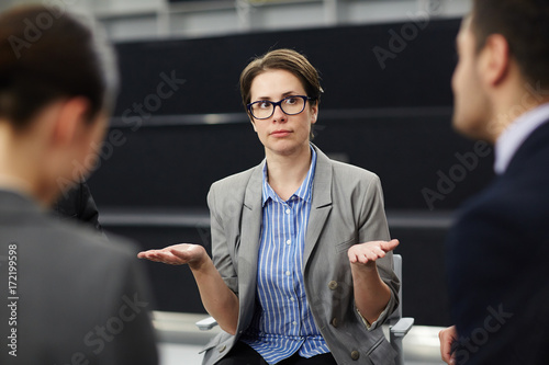 Unsure businesswoman with open palms looking at one of colleagues during conversation