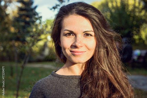 Autumn portrait of a happy beautiful woman with brown hair in city. Attractive brunette woman hipster style wearing white coat and grey pullover. Autumn atmosphere, nature and freedom concept.
