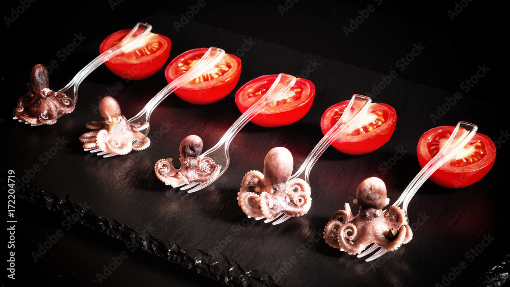 Closeup octopus appetizer of marinated seafood on a fork for canapes and tomatoes on a black background. Closeup octopus appetizer of marinated seafood on a fork for canapes and tomatoes on a black background.