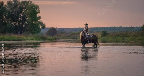 Slow motion 240fps shot of cowboy girl riding horse in water of sunset river