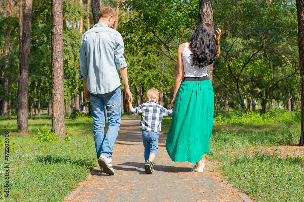 Dad and mom hold their son by the hand and walk along the park road. Family resting in the park