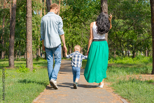 Obraz na płótnie Dad and mom hold their son by the hand and walk along the park road. Family resting in the park w salonie