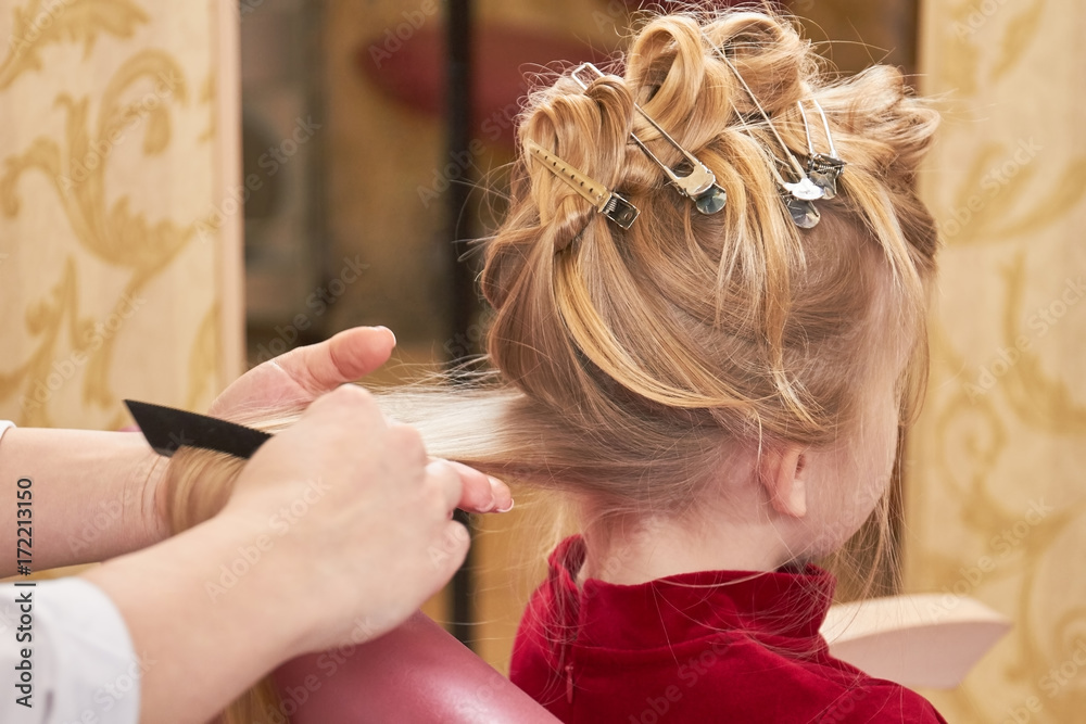 Fototapeta premium Little girl getting hair done. Hands of hairstylist working.