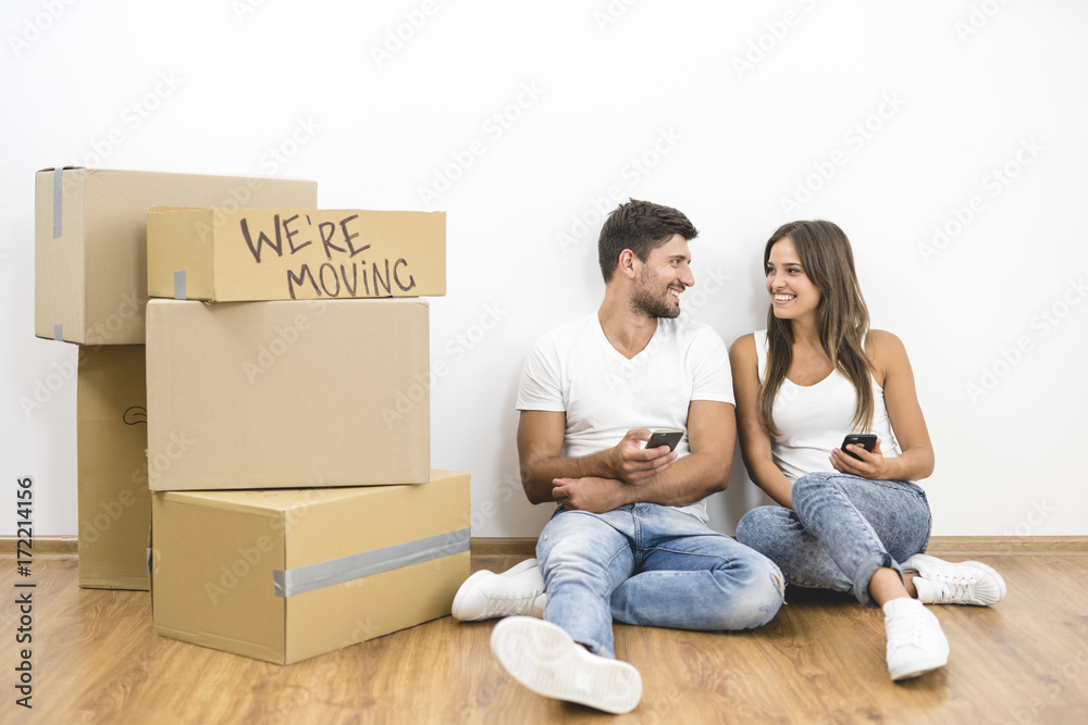 The happy couple phone near boxes on the background of the white wall The happy couple phone near boxes on the background of the white wall