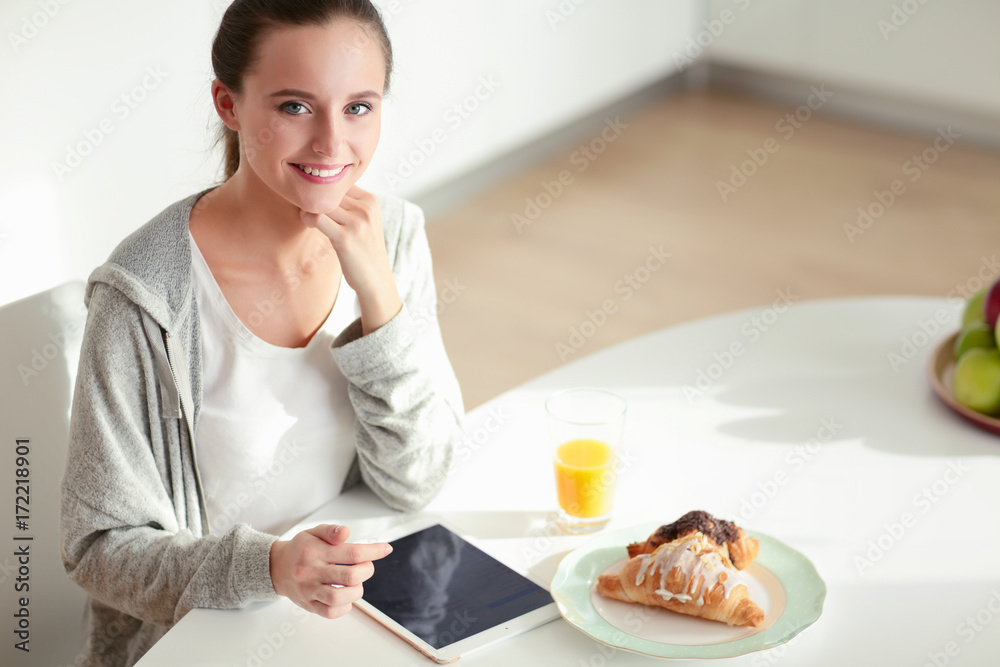 Young woman with orange juice and tablet in kitchen.