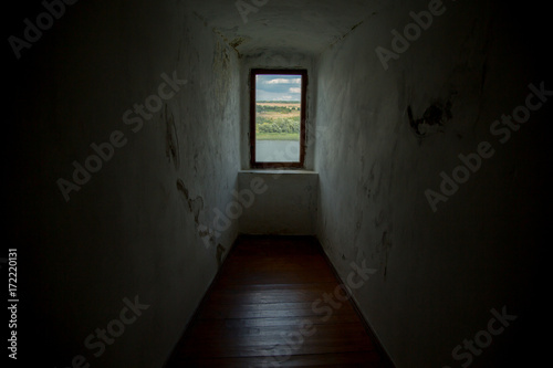 A window in the ancient castle wall, a view of a sunny day of summer forest, a hill, and a river.