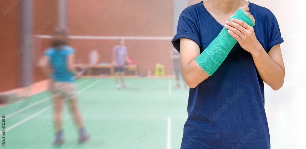 injury from sport, woman player with green arm cast on blurred background players badminton