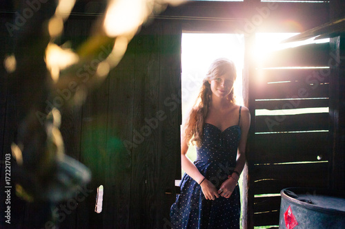 Young girl leaning against doorway of a rustic barn with the sunset behind her photo