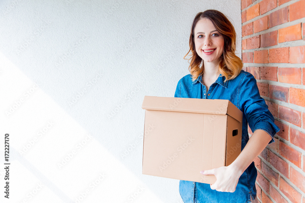 woman in jeans shirt standing on brick wall with moving box woman in jeans shirt standing on brick wall with moving box