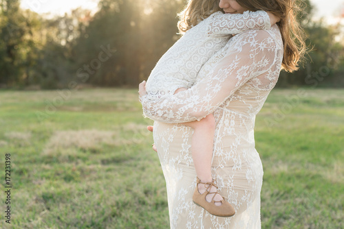 A Little Girl Hugs Her Daughter While Holding Her Pregnant Belly photo