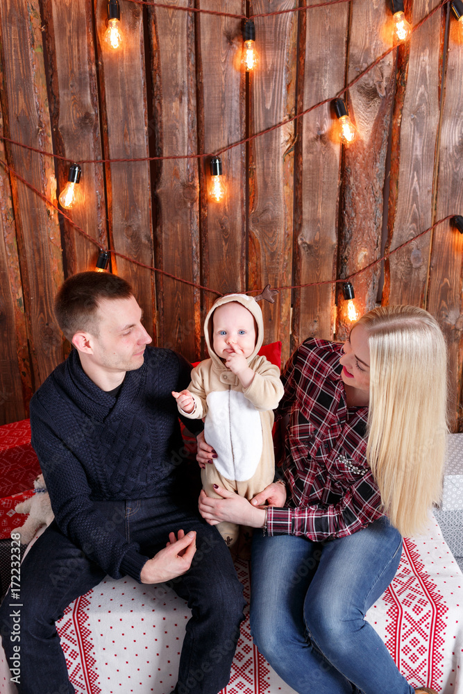 Happy family at Christmas. The parents and the baby sitting. Wall of wooden planks and garland