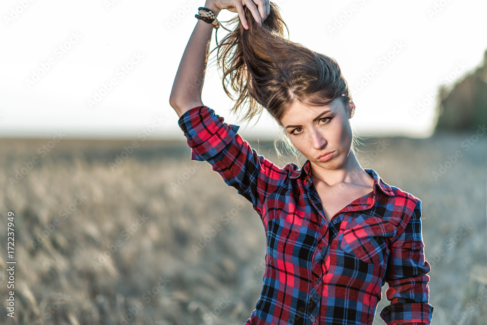 Beautiful girl field. Summer in nature. Happy holds her hair. In the evening shirt a brunette woman, close-up portrait. Fun playing with the hair, a concept of fun.