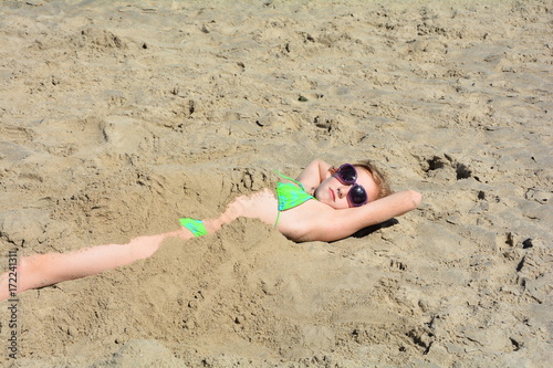 Halb eingegrabendes Mädchen am Sandstrand, mit Sonnenbrille und Arme hinterm Kopf