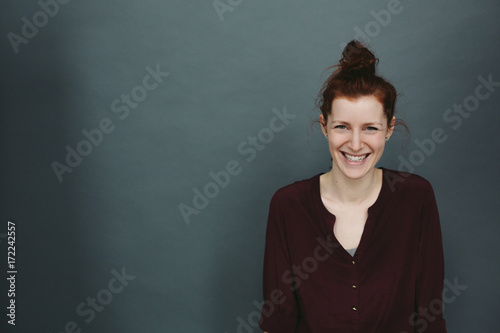 Happy candid portrait of young red head on solid grey blue background photo