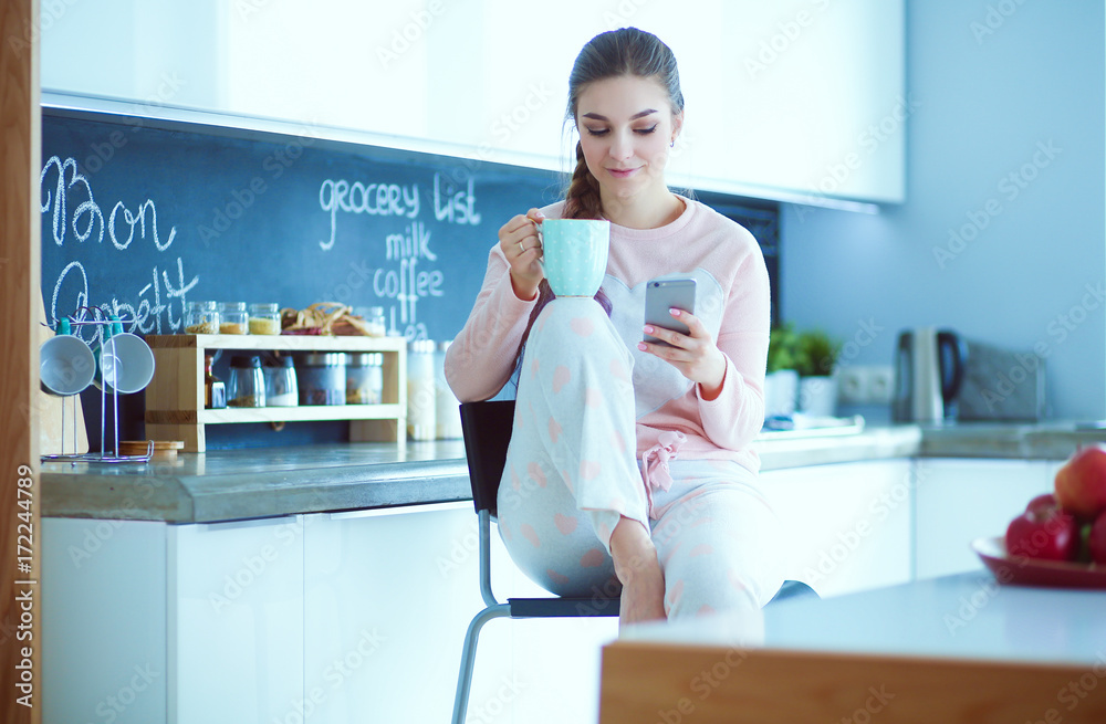 Woman using mobile phone sitting in modern kitchen. Woman using mobile phone sitting in modern kitchen.