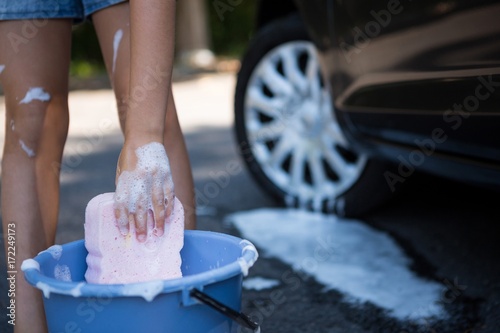 Teenage girl washing a car on a sunny day