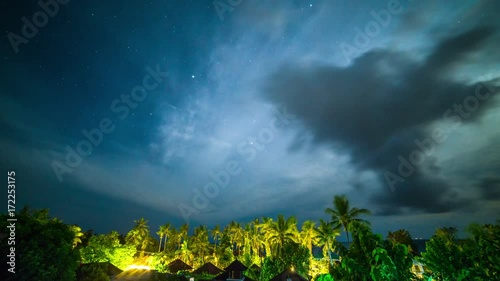 Night sky time-lapse of with stars over the rainforest, palms and bungalows on Bali island in Indonesia. photo