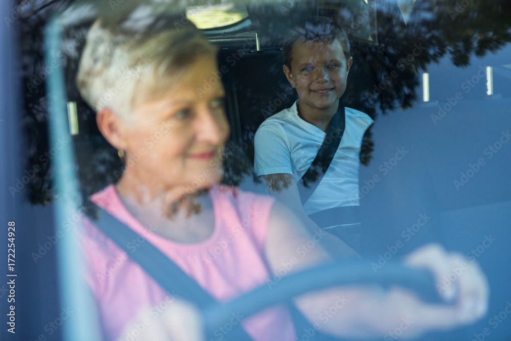 Grandmother driving a car while grandson sitting in the back Grandmother driving a car while grandson sitting in the back