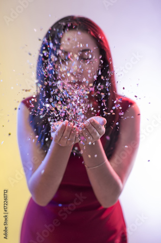 Beautiful girl on party background blowing confetti
