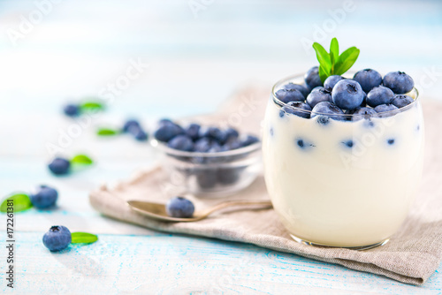 Clear jar of yogurt with blueberries over on wooden background