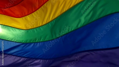 Rainbow flag flying in slow motion backlit against the sky