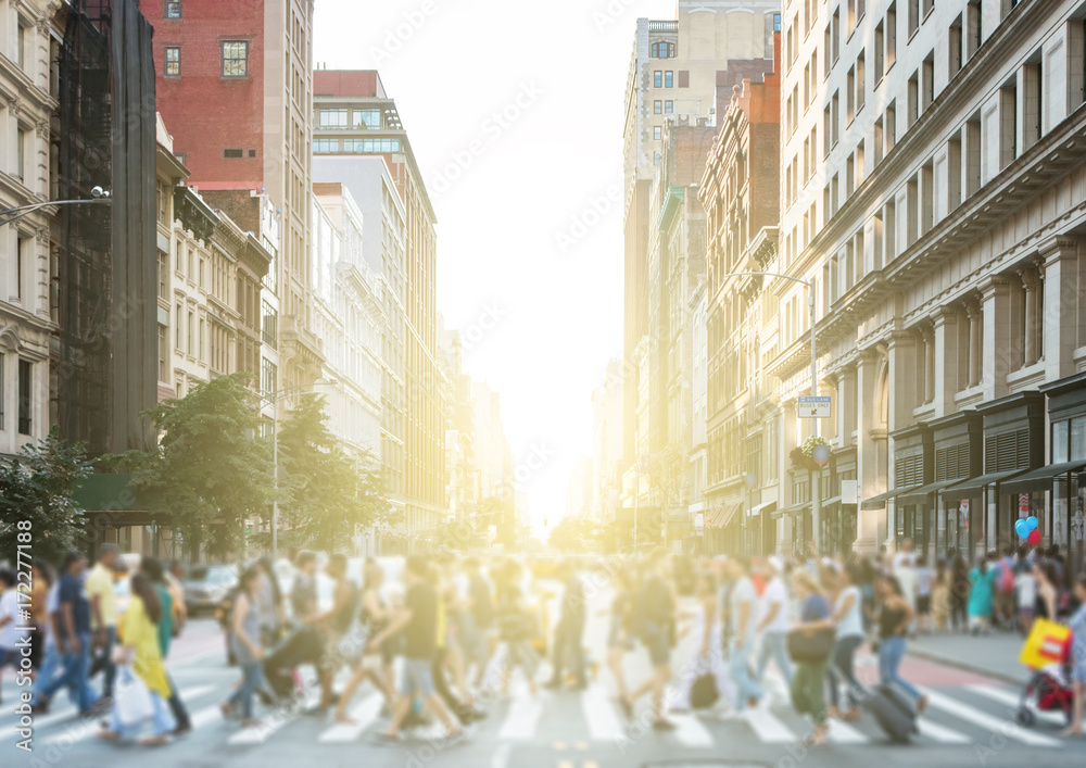 Crowds of colorful diverse people walking across a busy intersection in New York City with the light of the sun glowing in the background