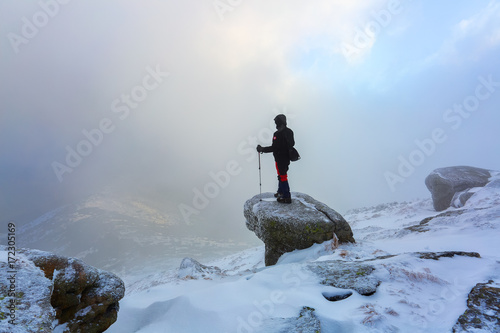 On a foggy winter day a guy with the travel sticks stands on the frozen stone and watches the fog.