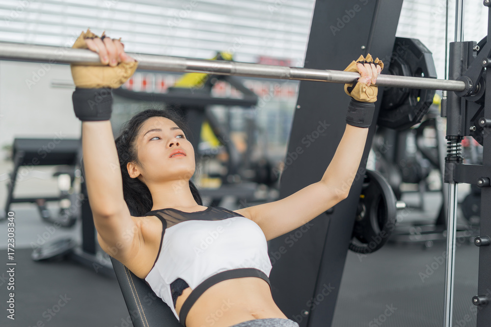 Fitness woman in training showing exercises with barbells in gym