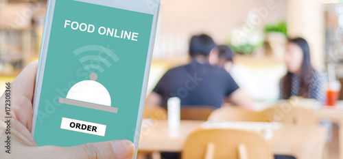 Hand holding smart phone with food online device on screen over blur restaurant background, banner wuth copy space, food online, food delivery concept