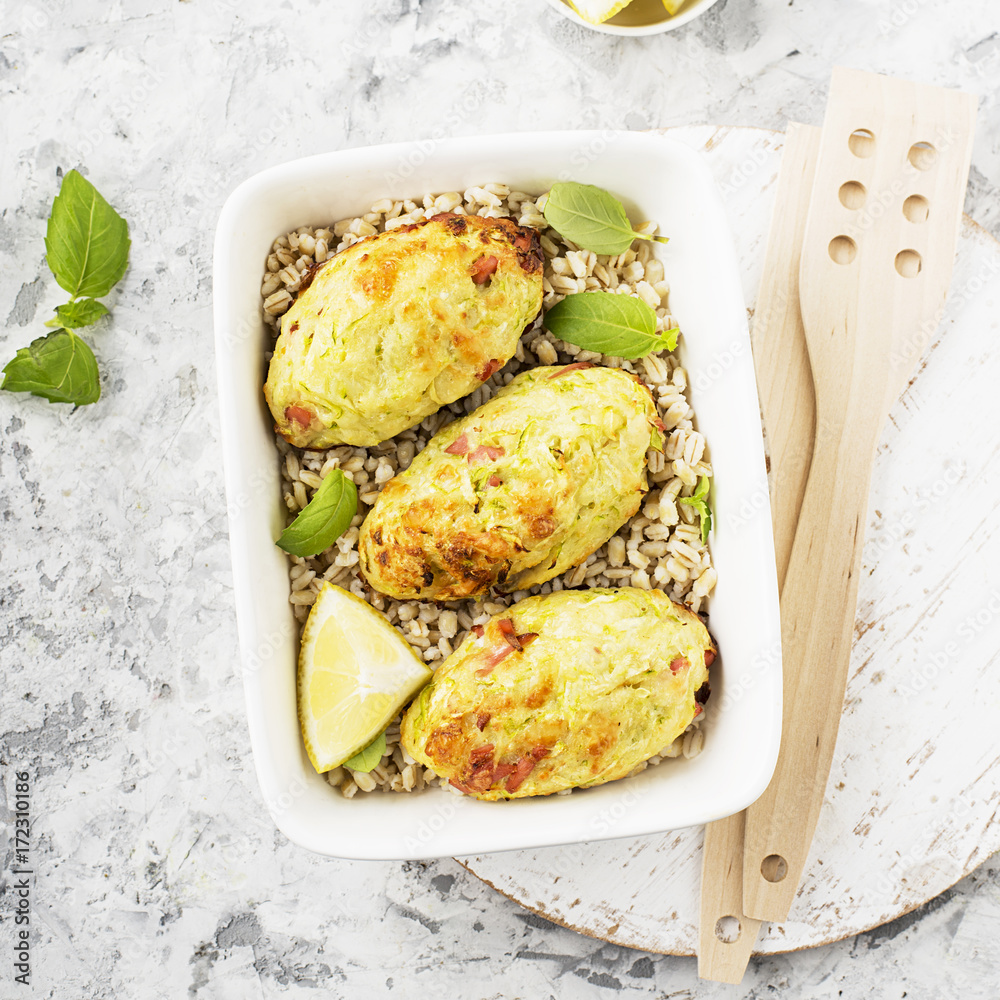 Fotografie Fritters with zucchini, potatoes with cheese and slices of baked bacon with a garnish of pearl barley in a baking dish