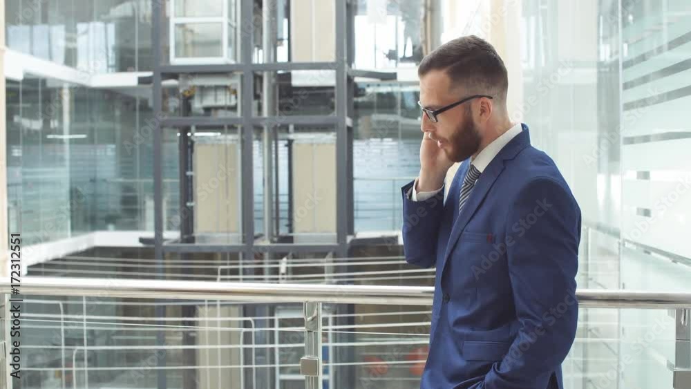 Young businessman uses smartphone, standing in business center. Young businessman uses smartphone, standing in business center.